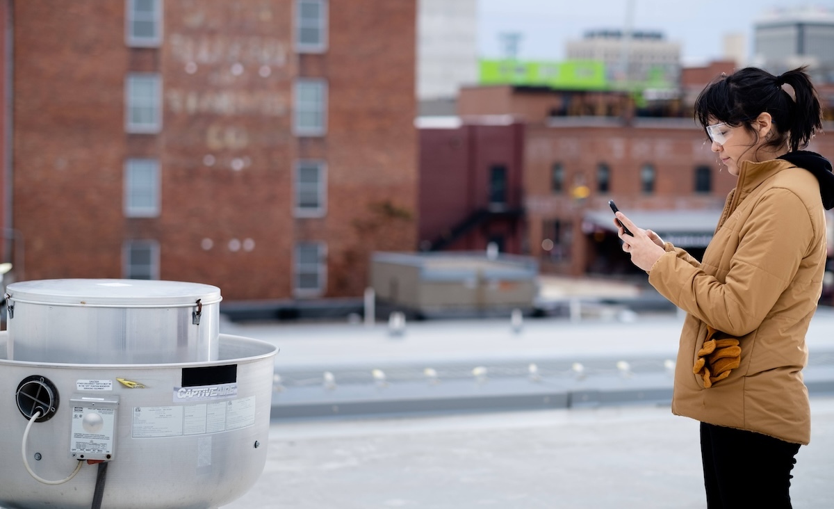 Woman inspecting rooftop HVAC unit and taking notes on smartphone