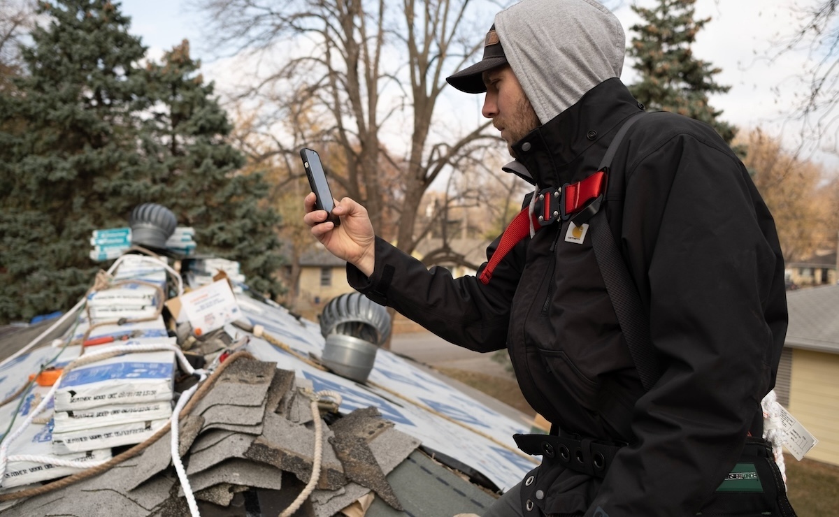 Roofing contractor taking a photo of roof shingles with smartphone