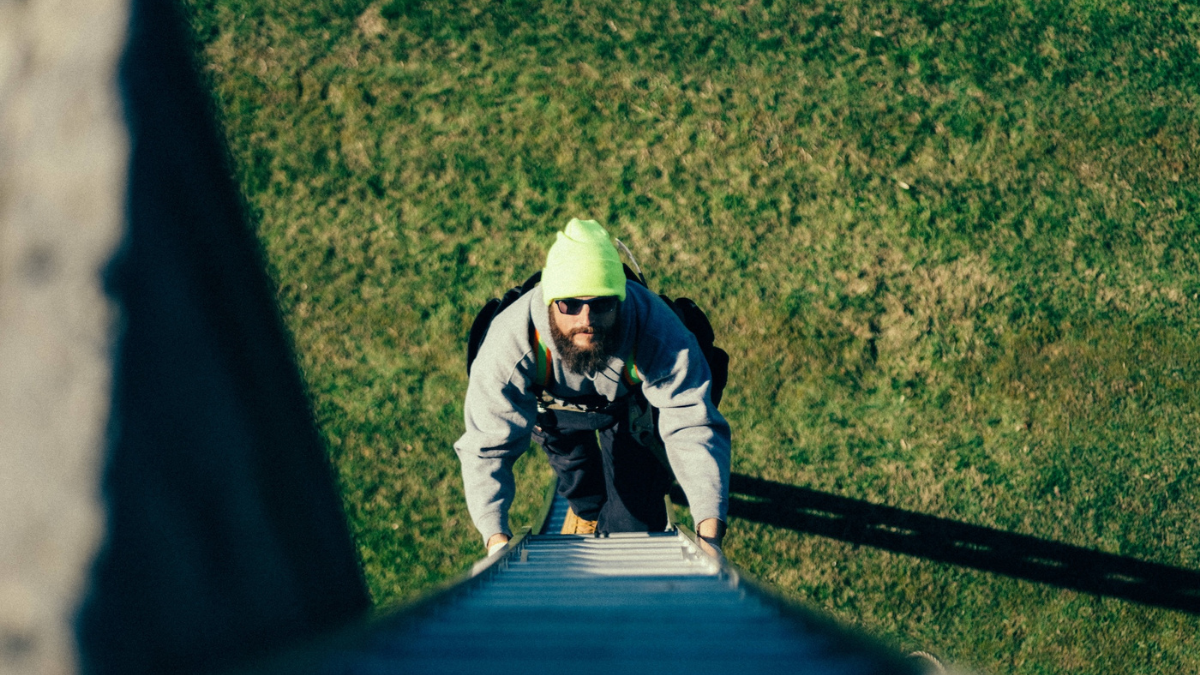 Roofing field tech climbing a ladder at a job site.