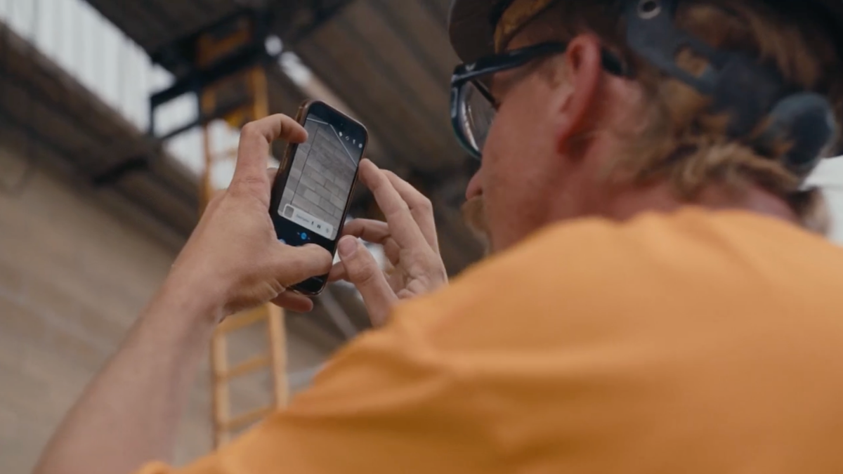 Worker photographing exterior work progress using smartphone.