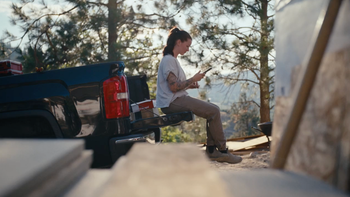 Contractor sits on the back of a truck tailgate at a job site using her phone to document progress