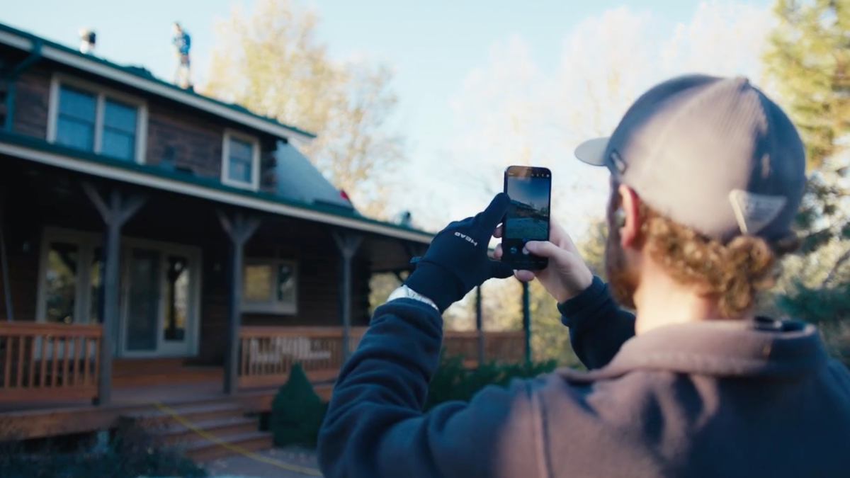 Contractor taking pictures of residential property exterior showing visible damage.