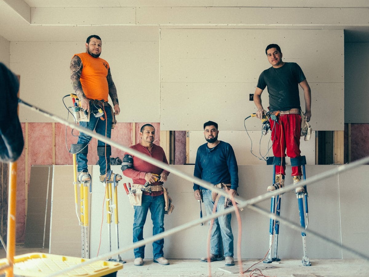 crew members on stilts and wearing tool belts while working on drywall installation