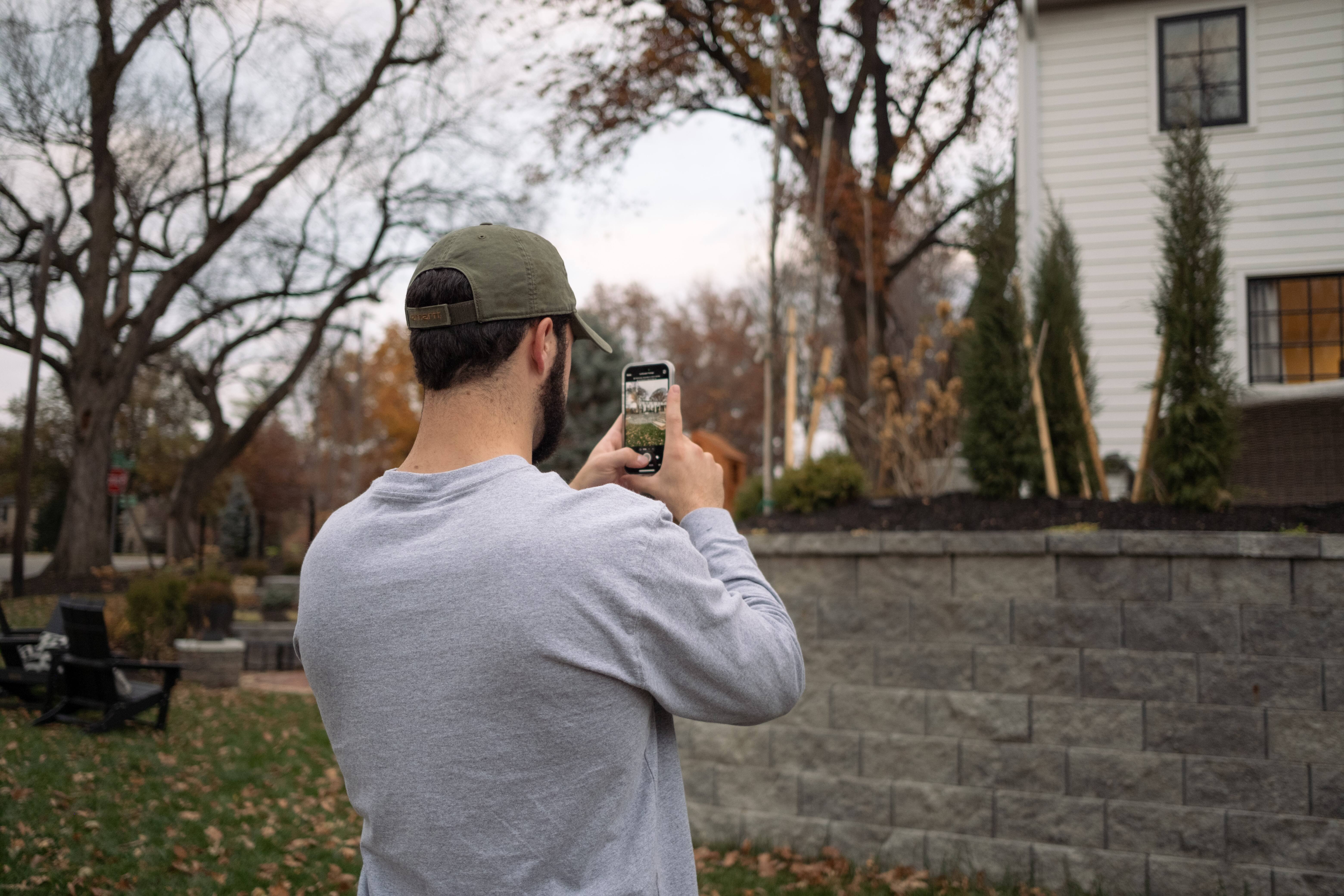 Contractor photographs exterior wall and landscaping with mobile app for job site documentation.