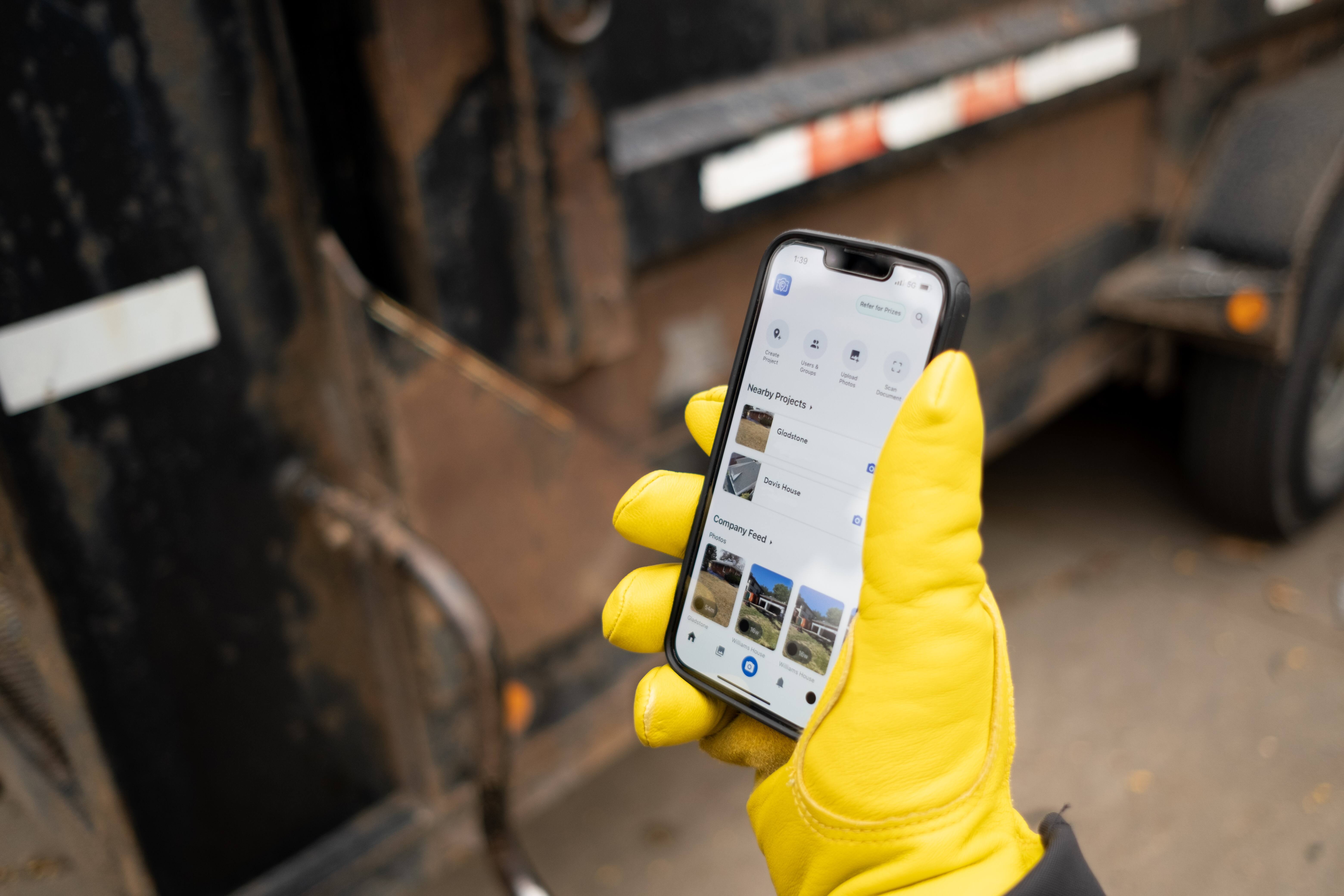 Worker wearing yellow gloves reviews project photos in mobile app on job site.