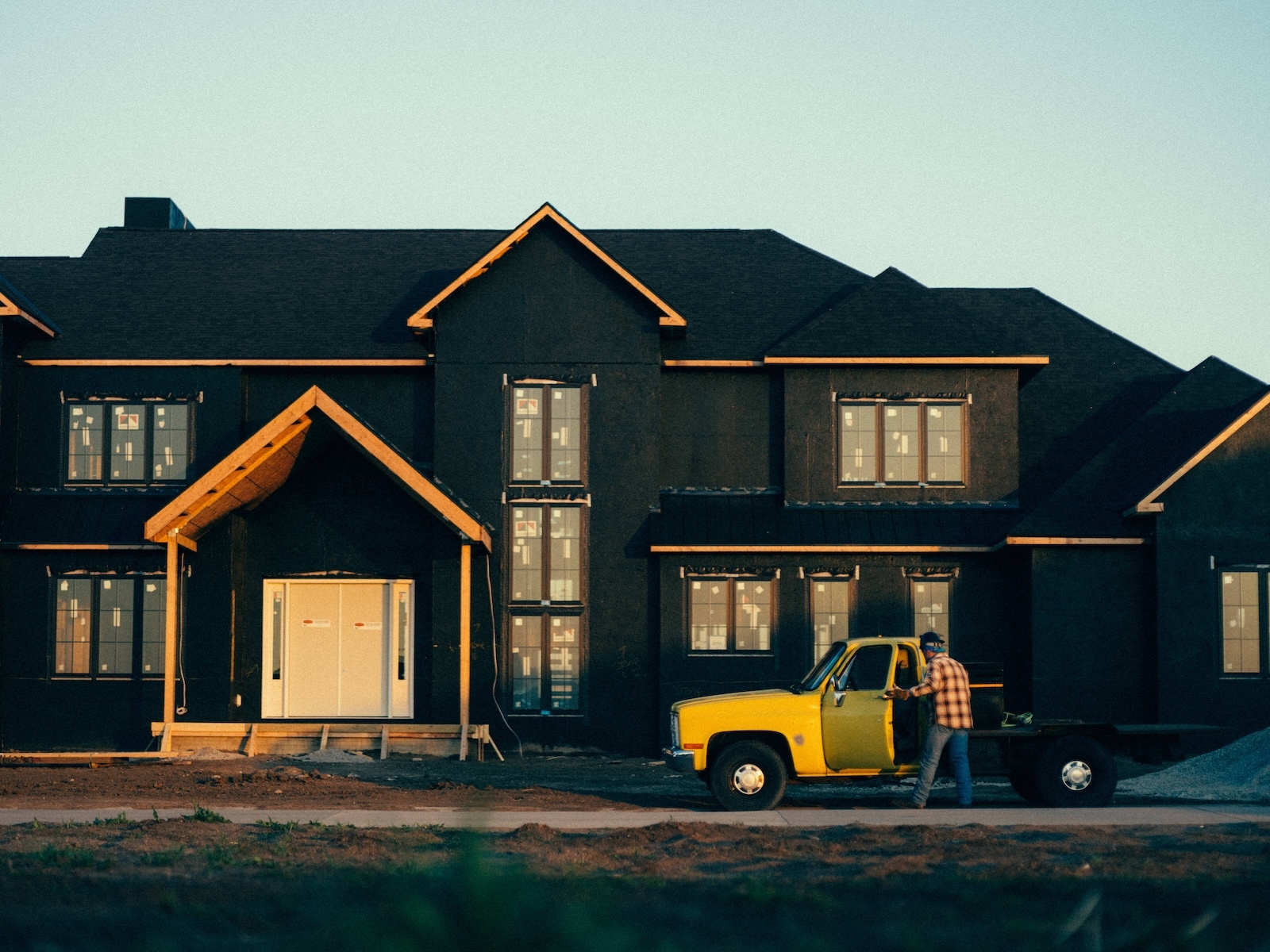 Contractor arrives at large residential build, stepping from yellow work truck onto active job site.