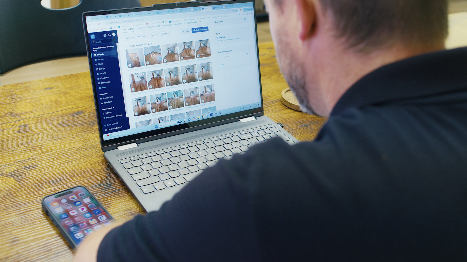 Contractor reviewing construction software dashboard with job site photos on a laptop in an office conference room.