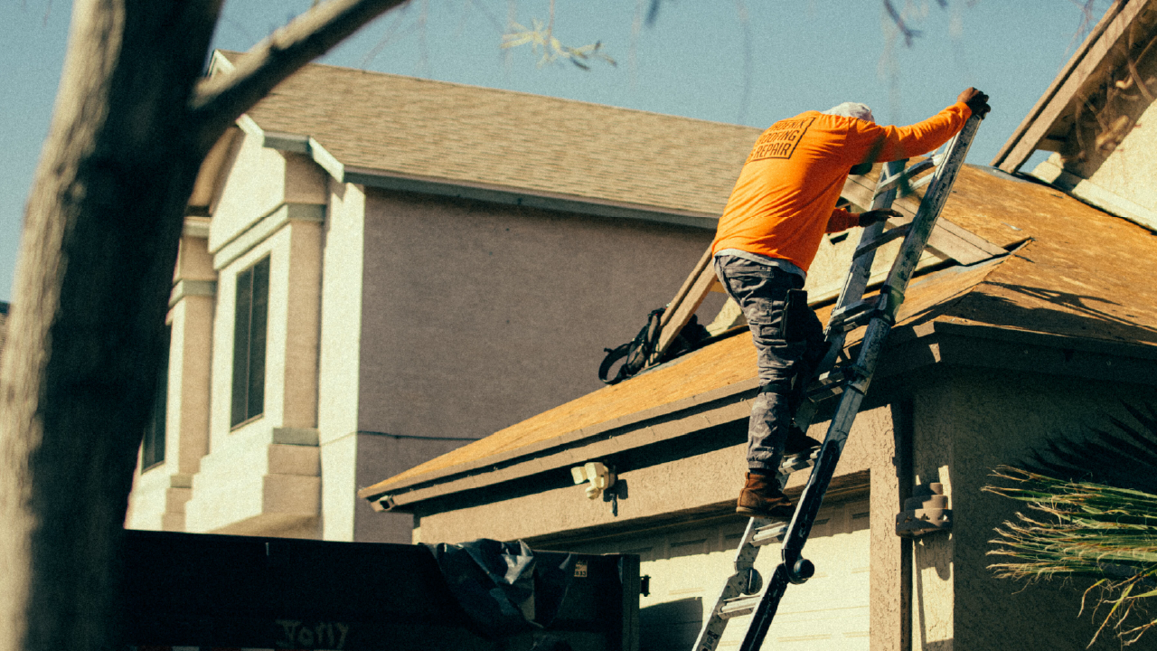 Construction worker climbs a ladder to work on a house roof.